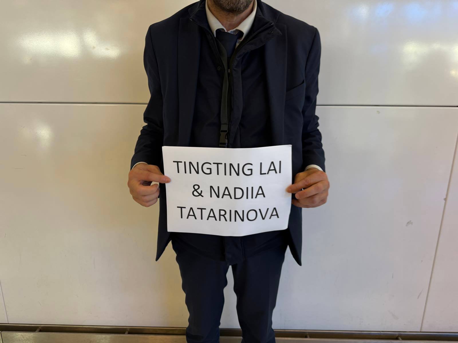 A driver holding a sign that reads TingTing Lai & Nadiia Tatarinova at the arrivals hall in Paris