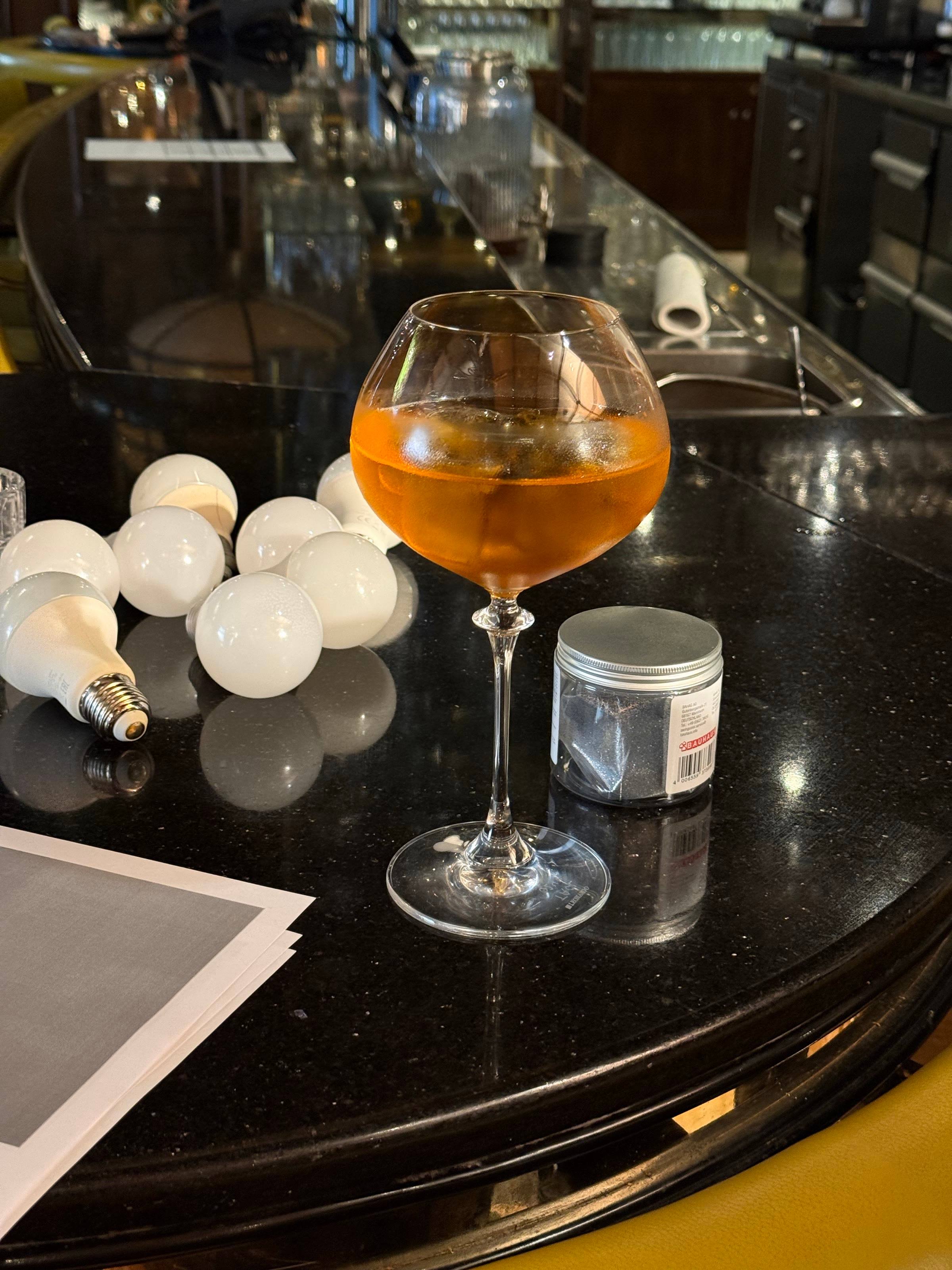 Ein Glas mit orangefarbenem Drink und das ausgedruckte Skript auf dem Tresen der Hotelbar zwischen zwei Takes