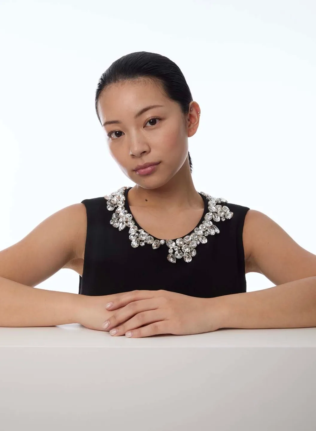 TingTing Lai in einem schwarzen Top mit Kristallkragen, die Arme auf einem weißen Sockel (visie.io)
