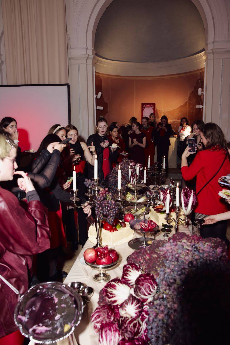 Guests in red photograph the long table with candles, grapes and radicchio