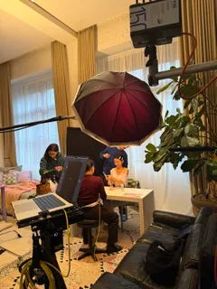 Hair und Make-up an einem Tisch unter einem roten Schirmlicht, daneben ein Laptop