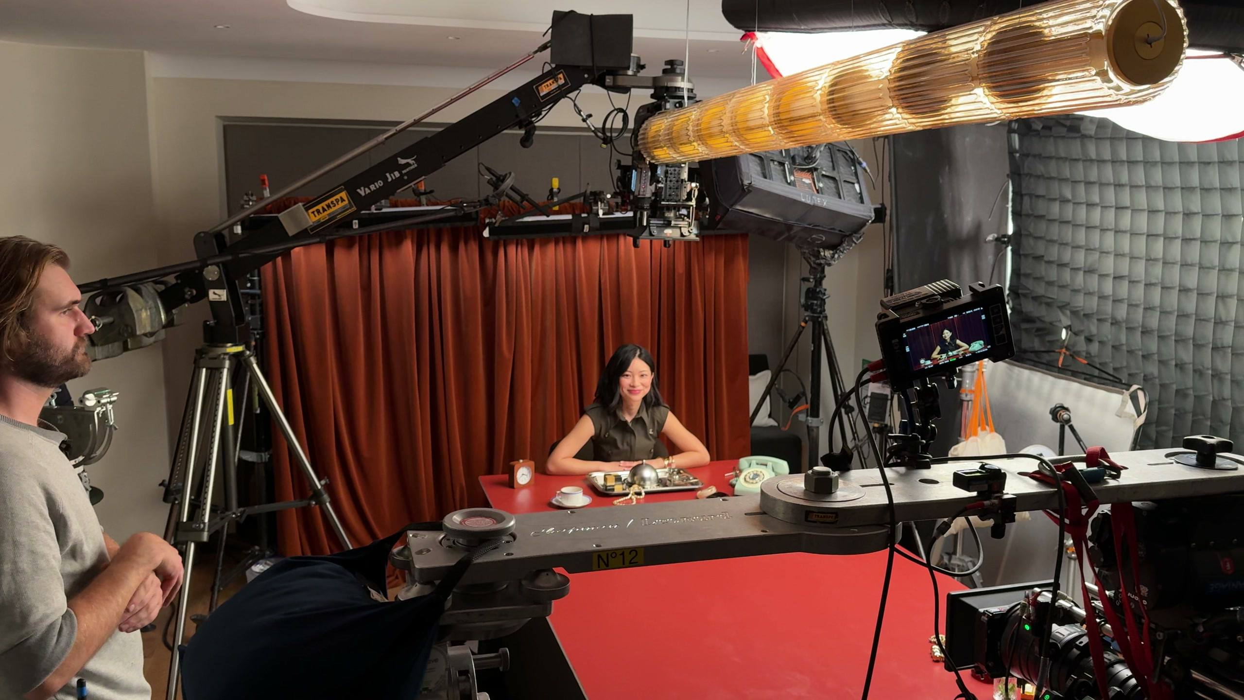 TingTing Lai at the red table on the Kilian Paris set, the camera crew around her