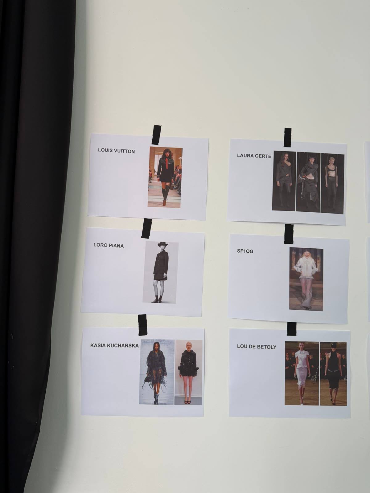 Printed looks taped to the studio wall, labelled by designer