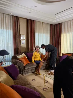 Aliona Gris in einem gelben Anzug auf einem Sofa in der Hotelsuite, die Crew neben ihr