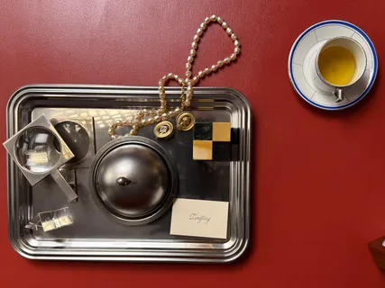 Ein Silbertablett mit Cloche, Perlen und Teetasse auf einem roten Tisch, von oben
